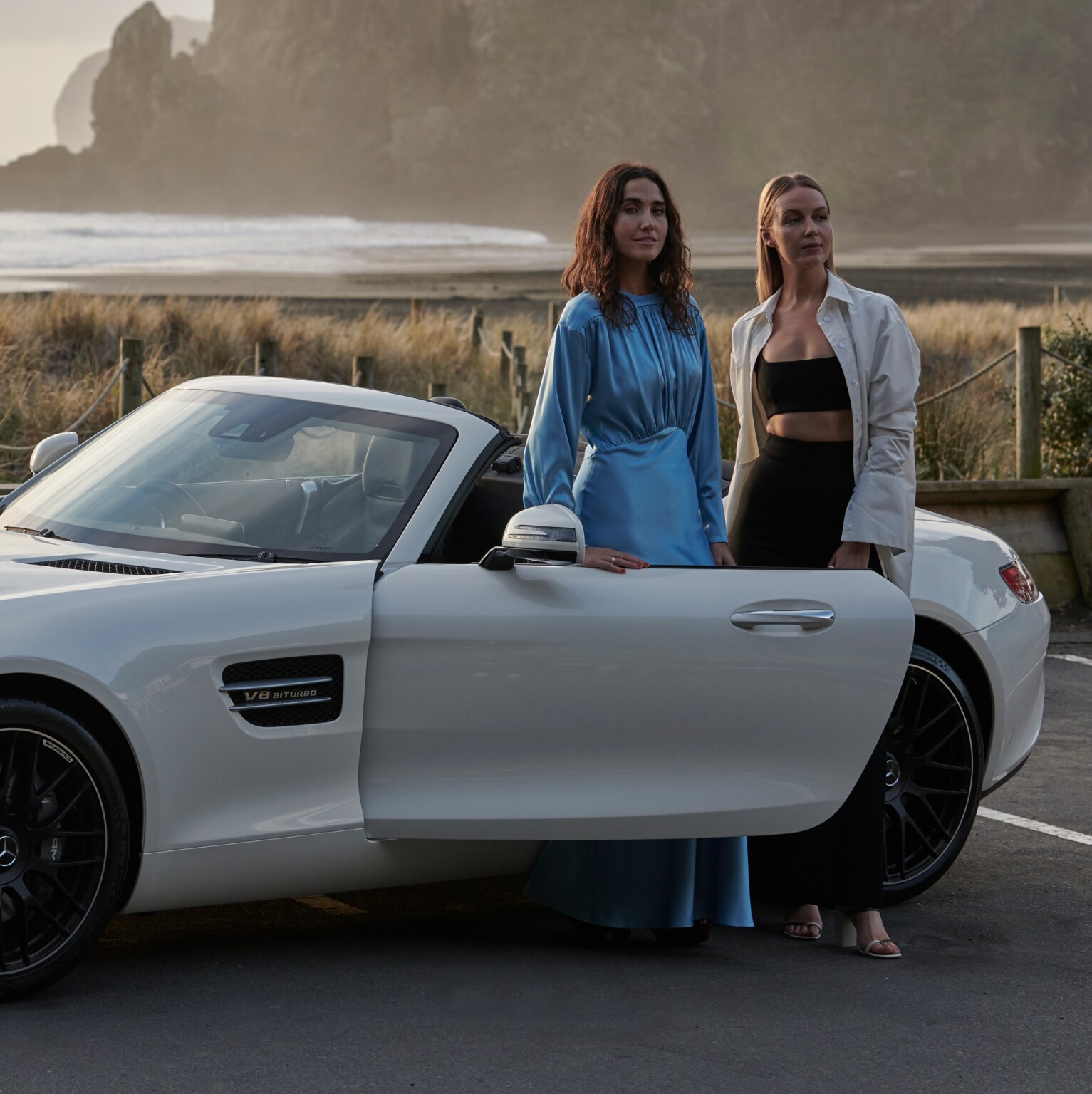 Two girls stand in front of a car 