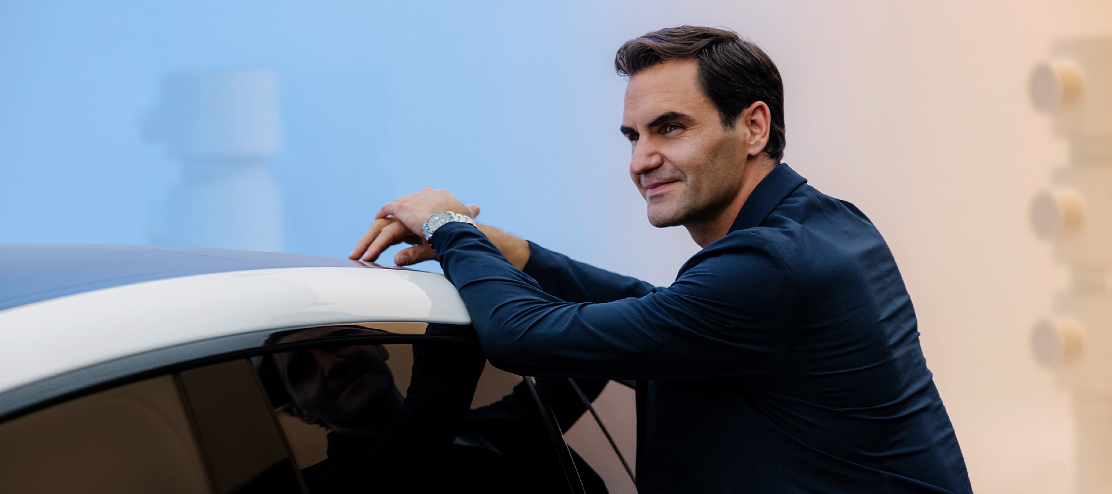 Roger Federer Roger Federer leaning against an all-electric Mercedes-Benz EQS Sedan and smiling.