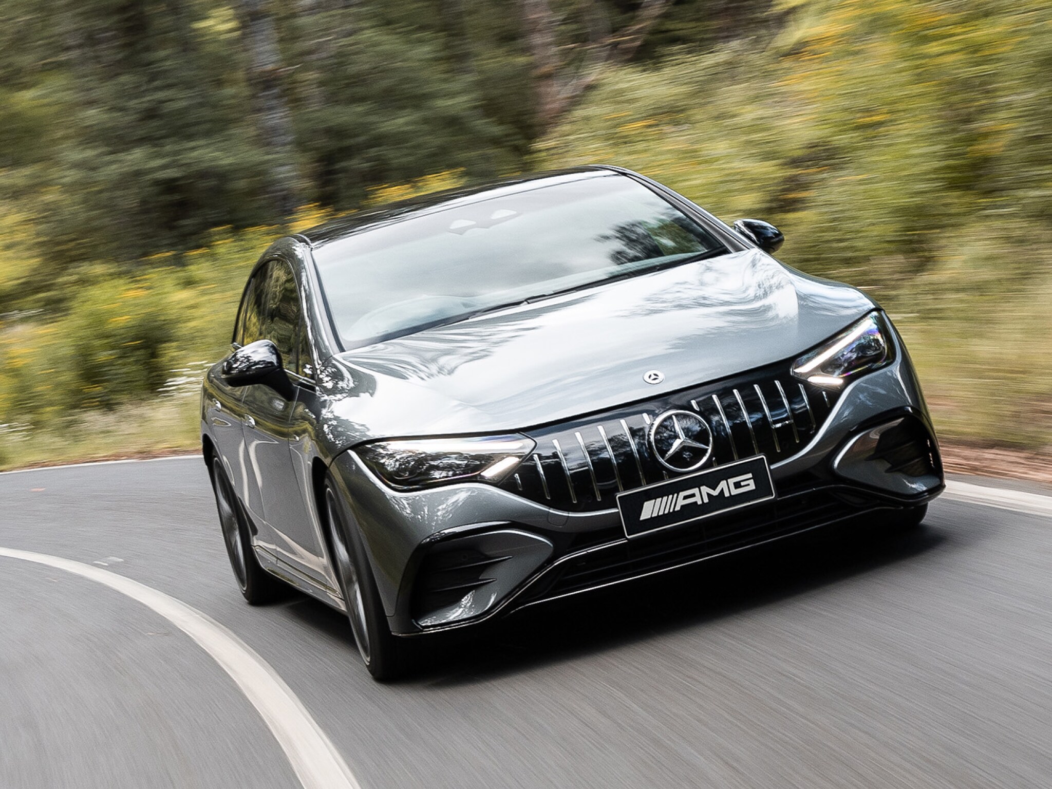 A grey all-electric Mercedes-AMG EQE 53 driving down a winding country road.