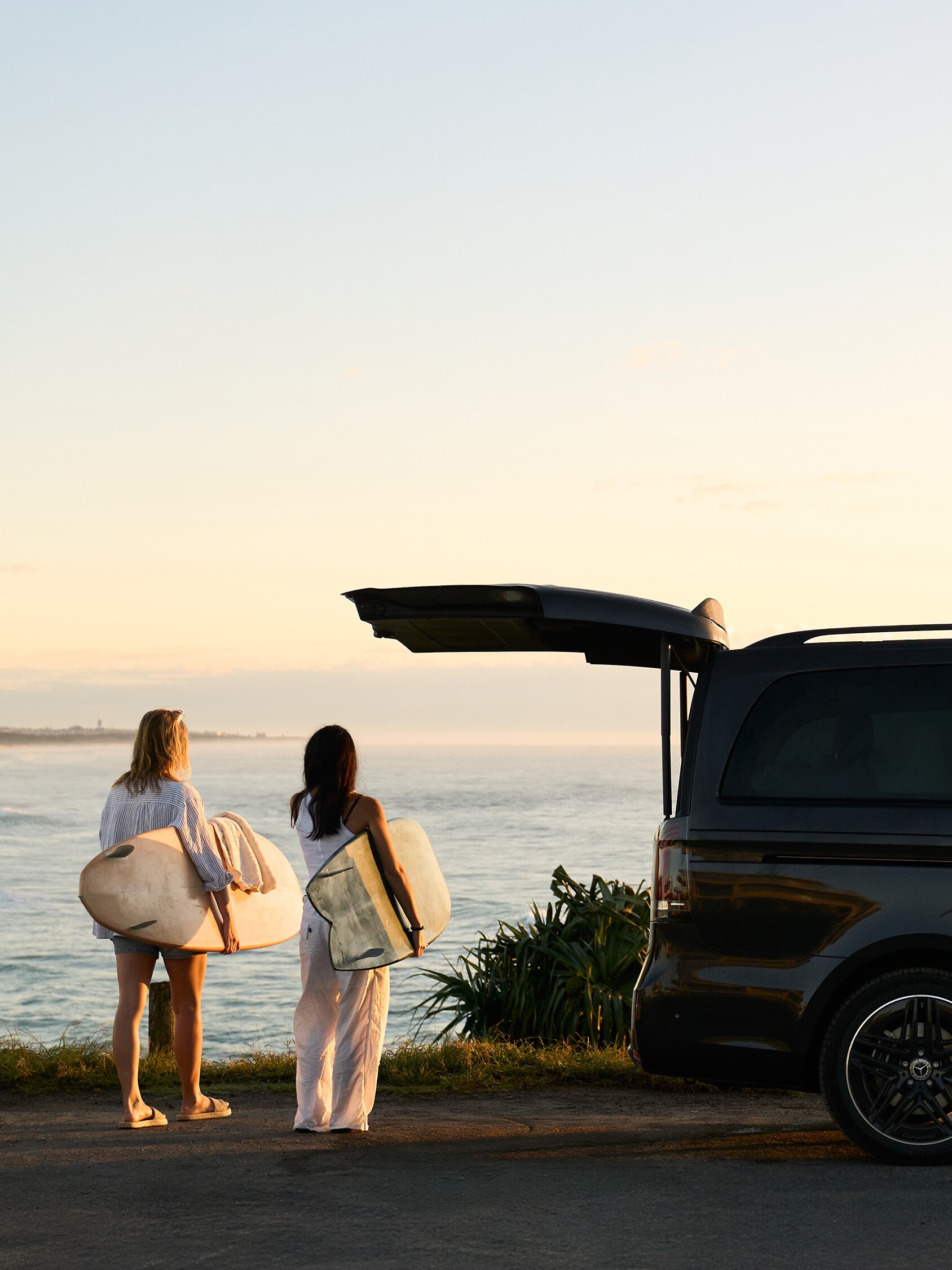 Two women with surfboards walking by beach.