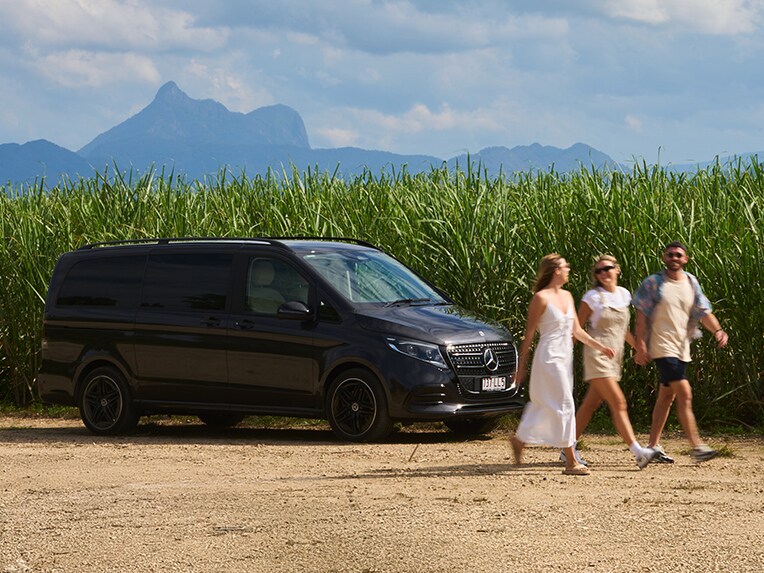 Three people walk past a van, against rural backdrop