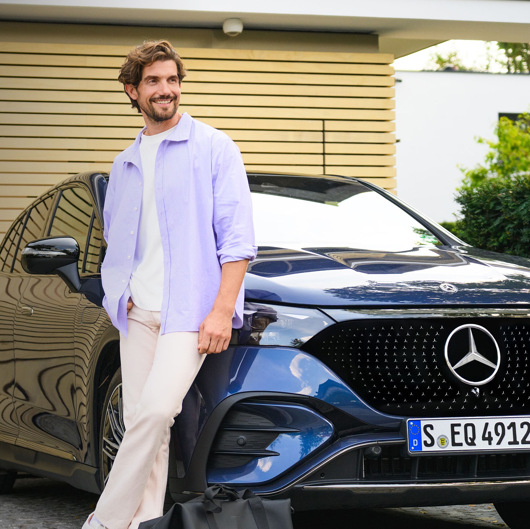 A person leaning against a Mercedes-Benz vehicle in front of their house.