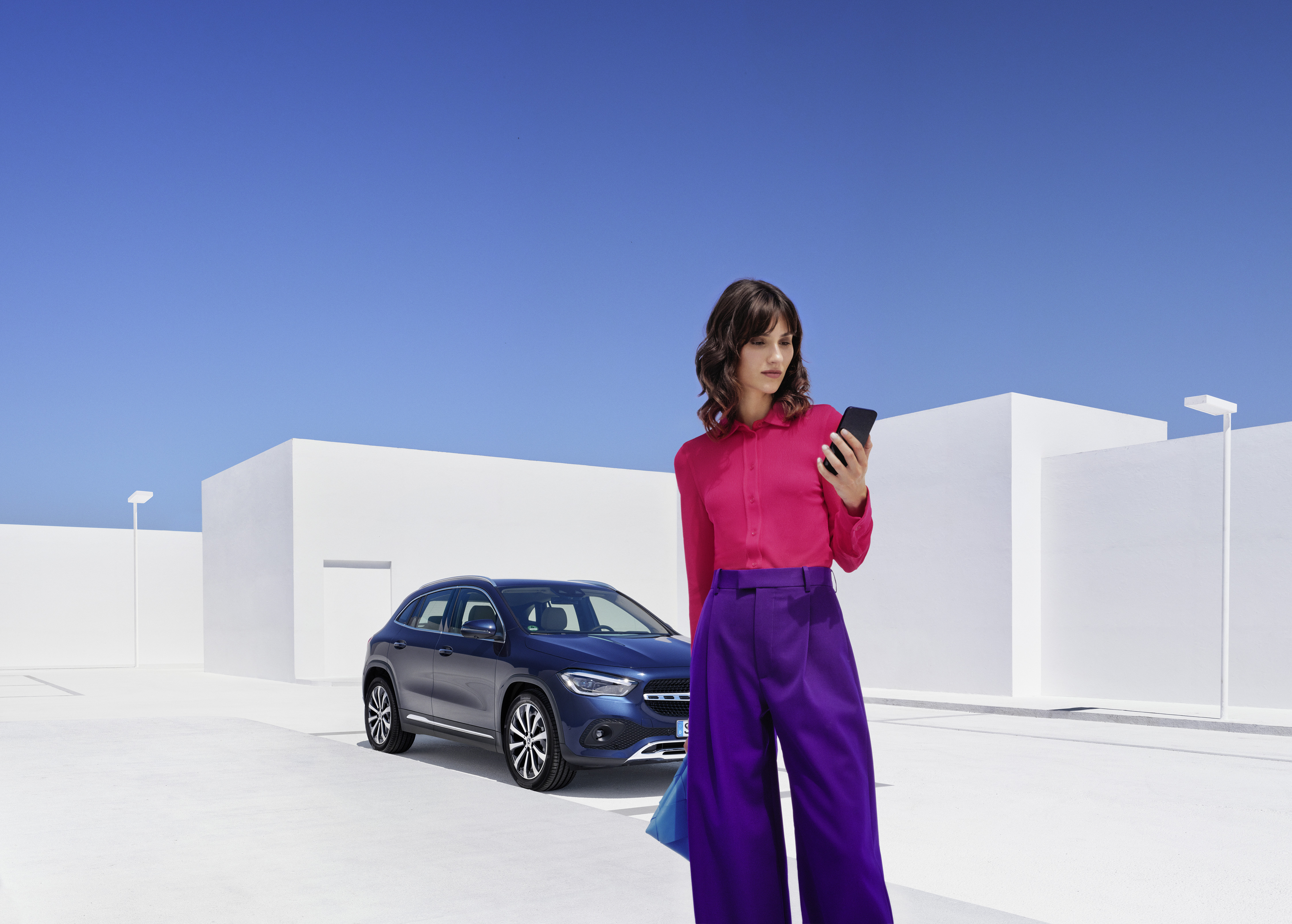 Breakdown Assistance | Mercedes-Benz A woman standing in front of a Mercedes-Benz looking at her smartphone.