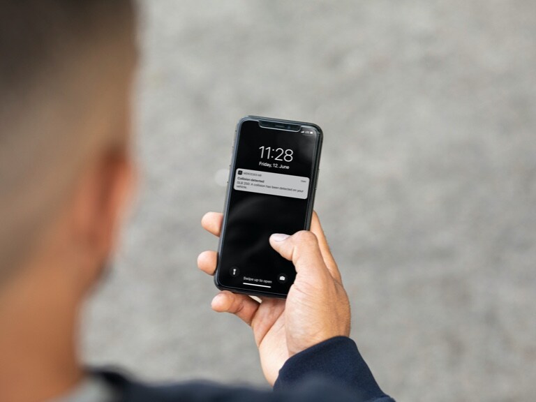 A man is informed by smartphone and the Theft notification and parking damage detection Digital Extra that a collision has occurred.
