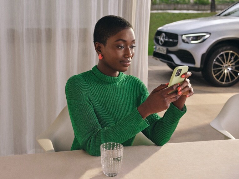 A woman looks at her smartphone, which is connected to her Mercedes-Benz via Digital Extras.