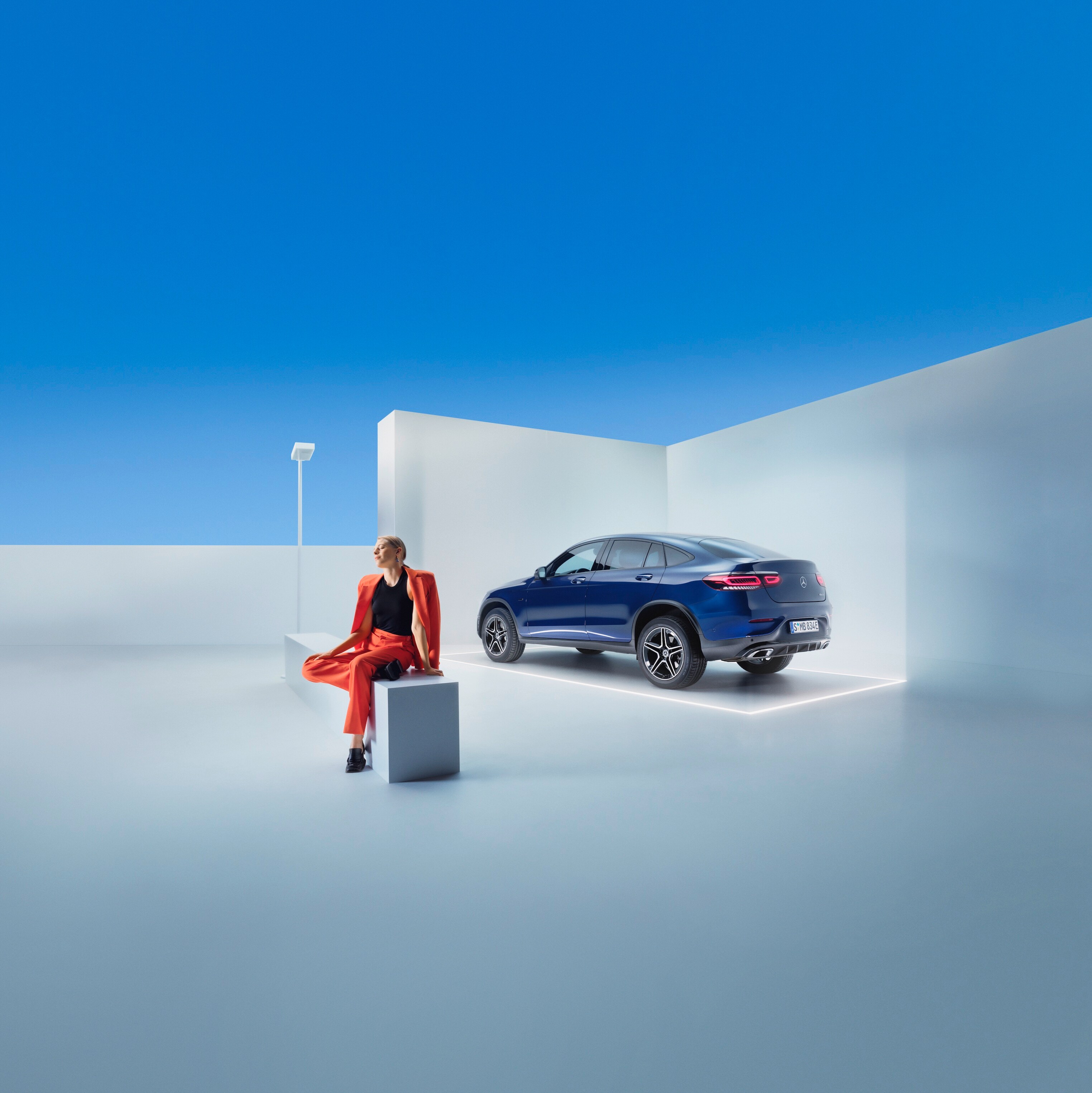 A woman sits on a bench in front of a Mercedes-Benz.