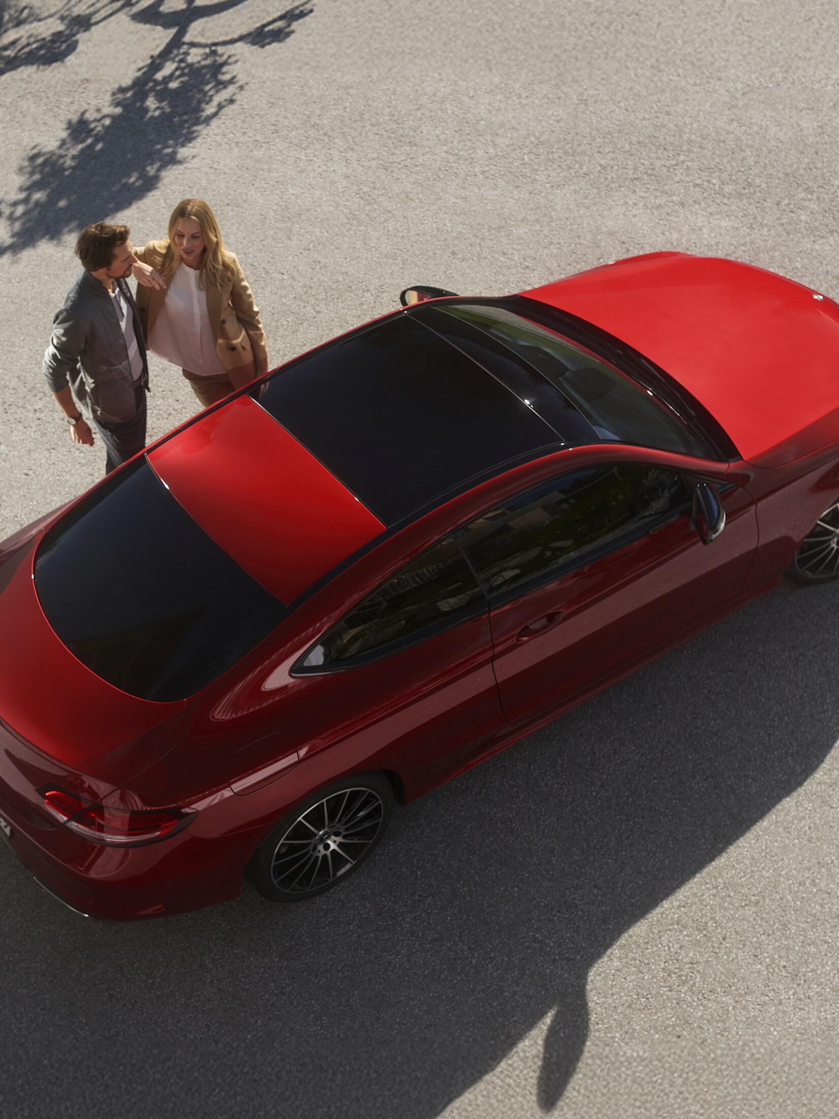 A man and woman standing next to a red Mercedes-Benz
