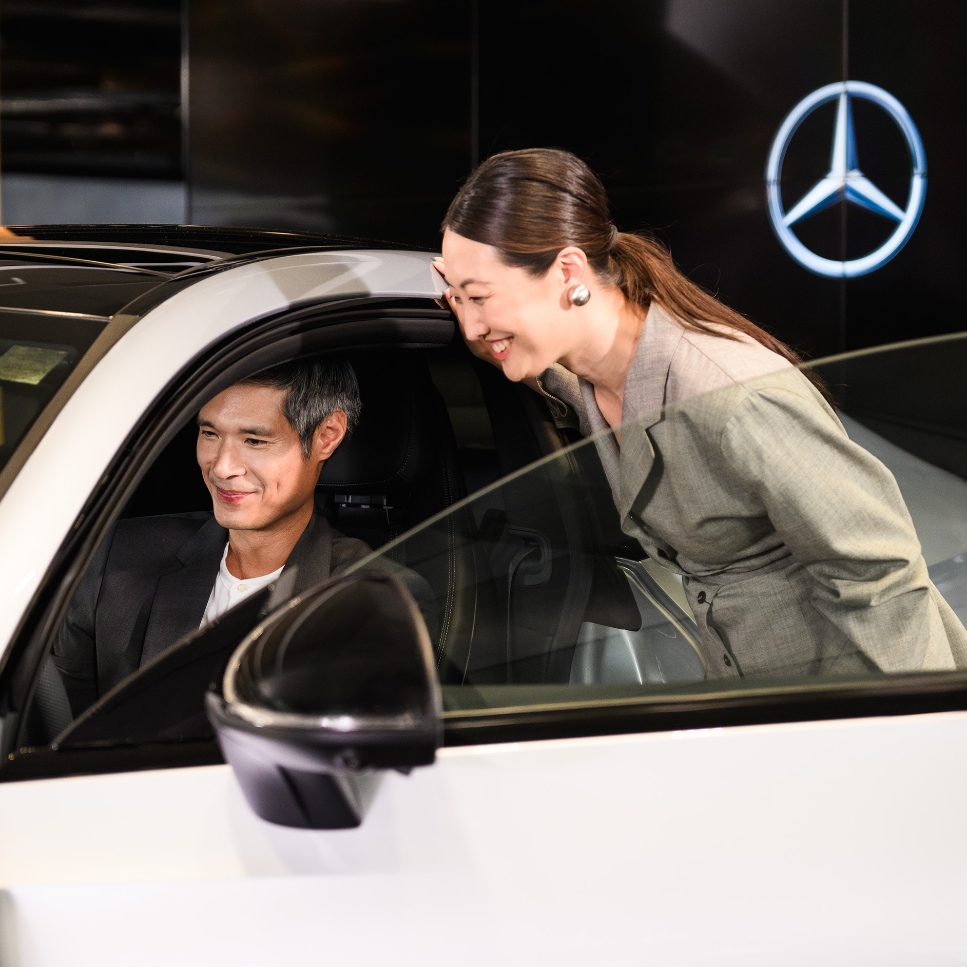 Speak to a Mercedes-Benz Finance expert. A person sitting in the driver’s seat of a Mercedes-Benz vehicle with someone looking inside the passenger side door open.